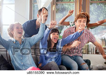Stock Image - Group of friends watching tv cheering. Fotosearch