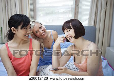 Group of young females on bed with mobile phone View Large Photo Image Stock Photograph - Group of young females on bed with mobile phone. Fotosearch