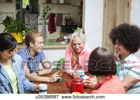 Group of young friends chatting around kitchen table View Large Photo Image Stock Photo - Group of young friends chatting around kitchen table. Fotosearch