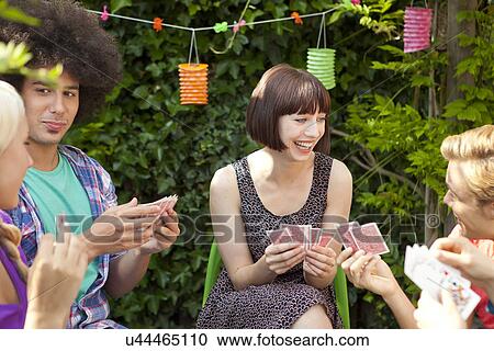 Stock Image - Group of young friends playing cards in garden. Fotosearch