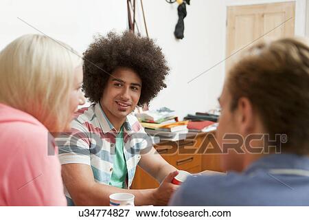 Stock Photo - Group of young friends sitting around kitchen table. Fotosearch