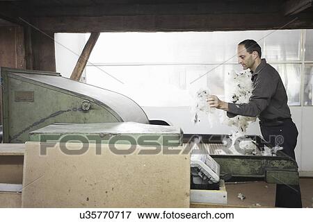 Stock Photo - Man adding fleece to machine in wool factory. Fotosearch