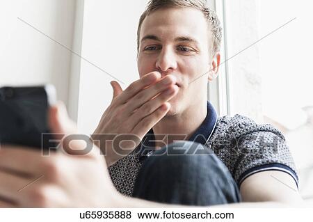 Stock Photo - Man blowing kiss at mobile phone. Fotosearch