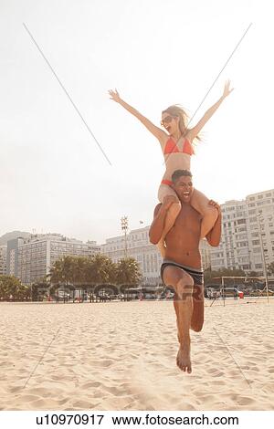 Stock Photo - Man carrying woman on shoulders running on Copacabana Beach, Rio de Janeiro, Brazil. Fotosearch