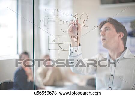 Man drawing architectural plans on glass wall, colleagues in background View Large Photo Image Stock Image - Man drawing architectural plans on glass wall, colleagues in background. Fotosearch
