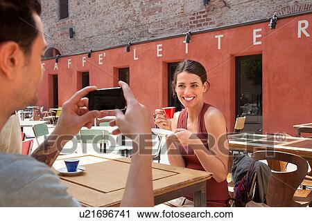 Stock Image - Man photographing woman outside cafe, Florence, Tuscany, Italy. Fotosearch