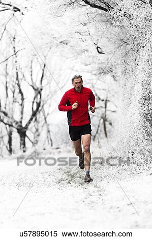Stock Photography - Man running through woods in winter, Wenlock Edge, Shropshire, England, UK. Fotosearch