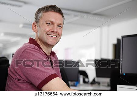 Man sitting at desk with computer, smiling at camera View Large Photo Image Picture - Man sitting at desk with computer, smiling at camera. Fotosearch