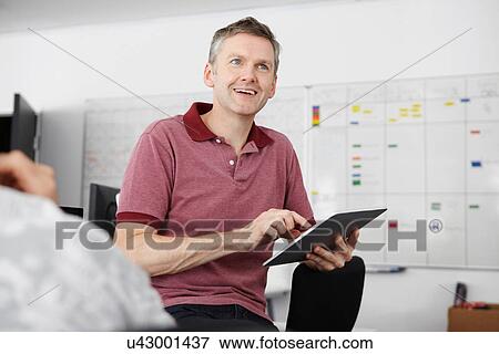 Man sitting in office using digital tablet View Large Photo Image Stock Photo - Man sitting in office using digital tablet. Fotosearch