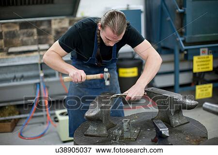 Stock Photo - Man using hammer for metalworking in creative studio. Fotosearch