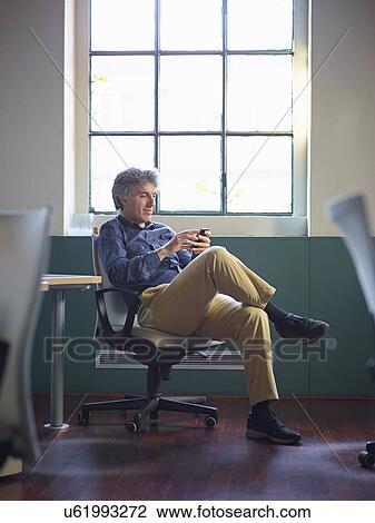 Stock Image - Mature businessman sitting on office chair wit cell phone. Fotosearch