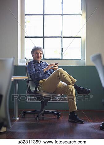 Stock Photo - Mature businessman sitting on office chair wit cell phone. Fotosearch
