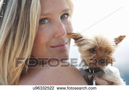 Stock Image - Mature woman holding pet dog, looking over shoulder. Fotosearch