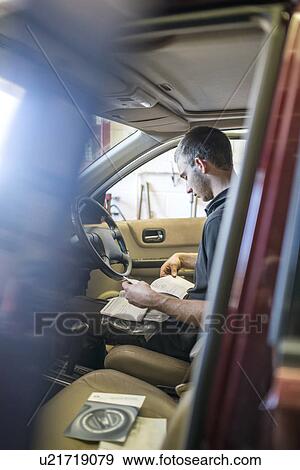 Mechanic sitting in driver's seat of car with manual View Large Photo Image Stock Photo - Mechanic sitting in driver's seat of car with manual. Fotosearch