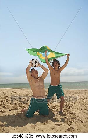Stock Photography - Men holding up brazilian flag on beach. Fotosearch