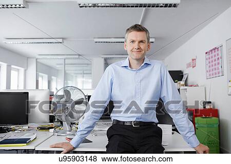 Men sitting on desk in office View Large Photo Image Stock Photo - Men sitting on desk in office. Fotosearch