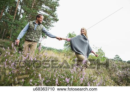 Stock Image - Mid adult couple holding hands in meadow. Fotosearch