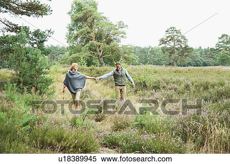 Stock Photography - Mid adult couple holding hands in meadow. Fotosearch