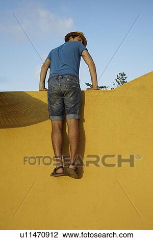 Mid adult man climbing over yellow wall View Large Photo Image Stock Image - Mid adult man climbing over yellow wall. Fotosearch