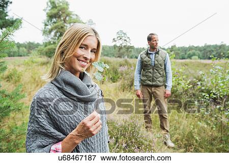 Stock Photo - Mid adult woman holding leaf, man in background. Fotosearch