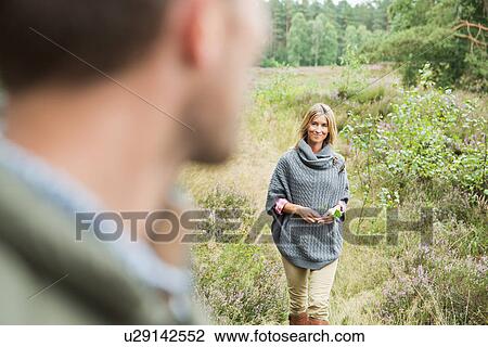 Mid adult woman holding leaf, man blurred in foreground View Large Photo Image Stock Image - Mid adult woman holding leaf, man blurred in foreground. Fotosearch