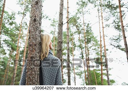 Stock Photo - Mid adult woman leaning against tree, low angle. Fotosearch