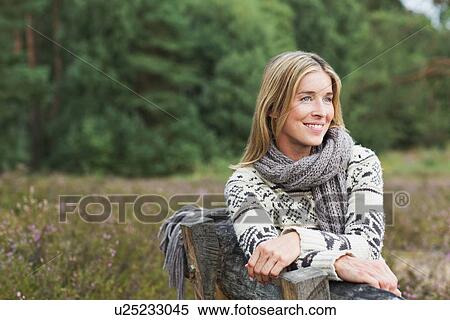 Mid adult woman wearing sweater on bench View Large Photo Image Stock Photography - Mid adult woman wearing sweater on bench. Fotosearch