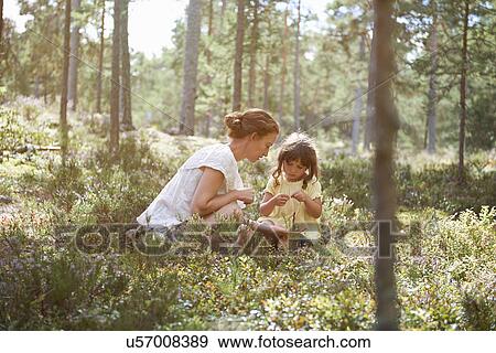 Stock Photo - Mother and daughter sitting in long grass looking at plants. Fotosearch