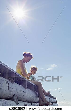 Stock Image - Mother and daughter sitting on pier, Utvalnas, Gavle, Sweden. Fotosearch