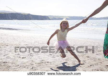 Stock Photo - Mother and daughter wearing tutu running on beach, Wales, UK. Fotosearch