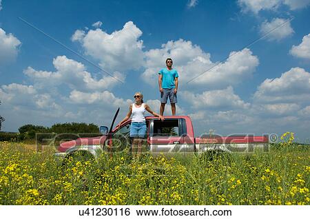 Stock Photograph - Mother and son with pickup truck in field, son standing on top of truck. Fotosearch