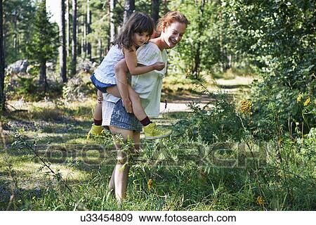 Stock Photo - Mother giving daughter piggy back through forest. Fotosearch