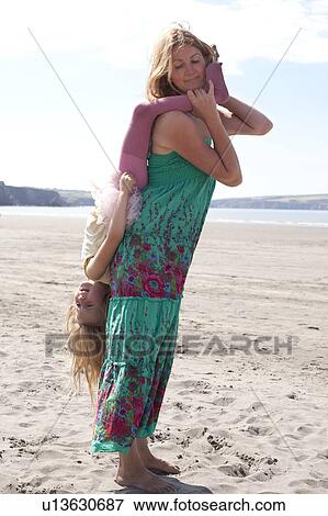 Stock Photo - Mother holding daughter upside down on beach, Wales, UK. Fotosearch
