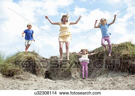 Picture - Mother with three children jumping off dunes, Wales, UK. Fotosearch