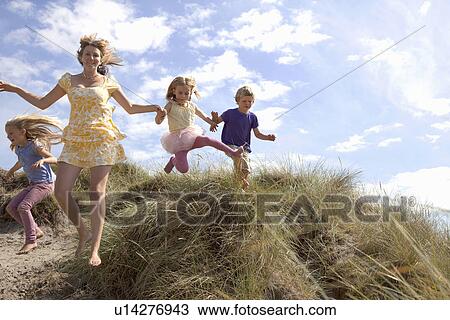 Stock Image - Mother with three children jumping off dunes, Wales, UK. Fotosearch