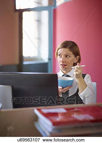 Stock Photo - Office worker eating breakfast cereal at desk. Fotosearch