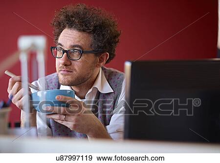 Office worker eating breakfast cereal at desk View Large Photo Image Stock Photo - Office worker eating breakfast cereal at desk. Fotosearch