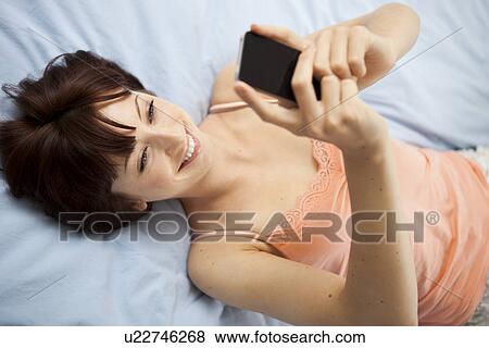 Overhead view of young woman on bed taking self portrait View Large Photo Image Stock Photo - Overhead view of young woman on bed taking self portrait. Fotosearch