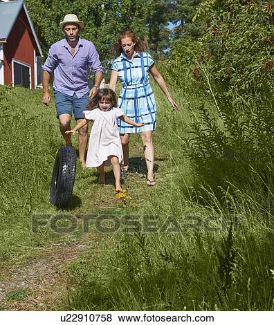 Stock Photo - Parents and girl rolling tyre on path, Utvalnas, Gavle, Sweden. Fotosearch