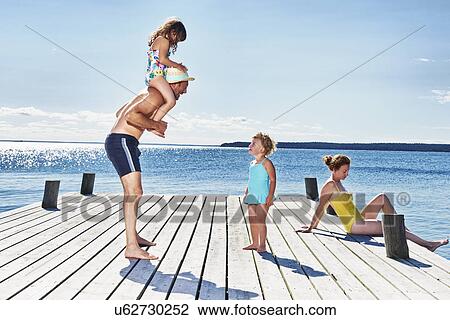 Stock Image - Parents and two young girls on pier, Utvalnas, Gavle, Sweden. Fotosearch