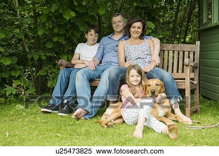 Stock Photography - Portrait of family with two children sitting on garden bench with dog. Fotosearch