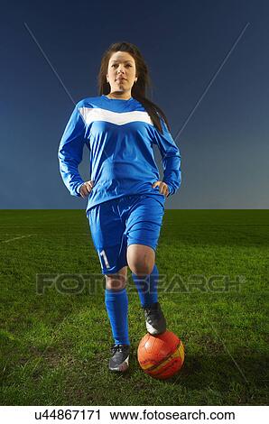 Stock Image - Portrait of female footballer with foot on ball. Fotosearch