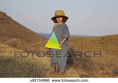 Stock Photograph - Portrait of girl holding triangle shape in field. Fotosearch