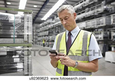 Stock Image - Portrait of manager using mobile phone in engineering warehouse. Fotosearch