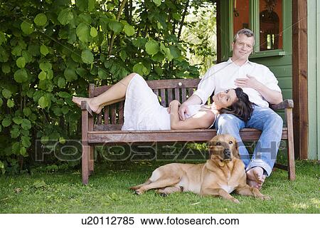 Stock Photography - Portrait of mature couple on garden bench with dog. Fotosearch