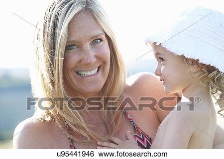 Stock Photograph - Portrait of mother holding young daughter wearing sunhat. Fotosearch