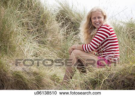 Stock Image - Portrait of teenage girl sitting on dunes, Wales, UK. Fotosearch