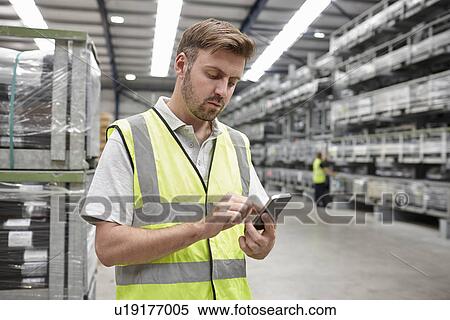 Stock Photography - Portrait of worker using mobile phone in engineering warehouse. Fotosearch