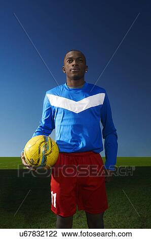Stock Image - Portrait of young man holding football. Fotosearch