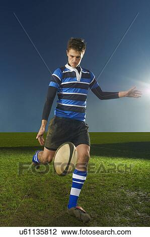 Stock Image - Portrait of young man kicking rugby ball. Fotosearch
